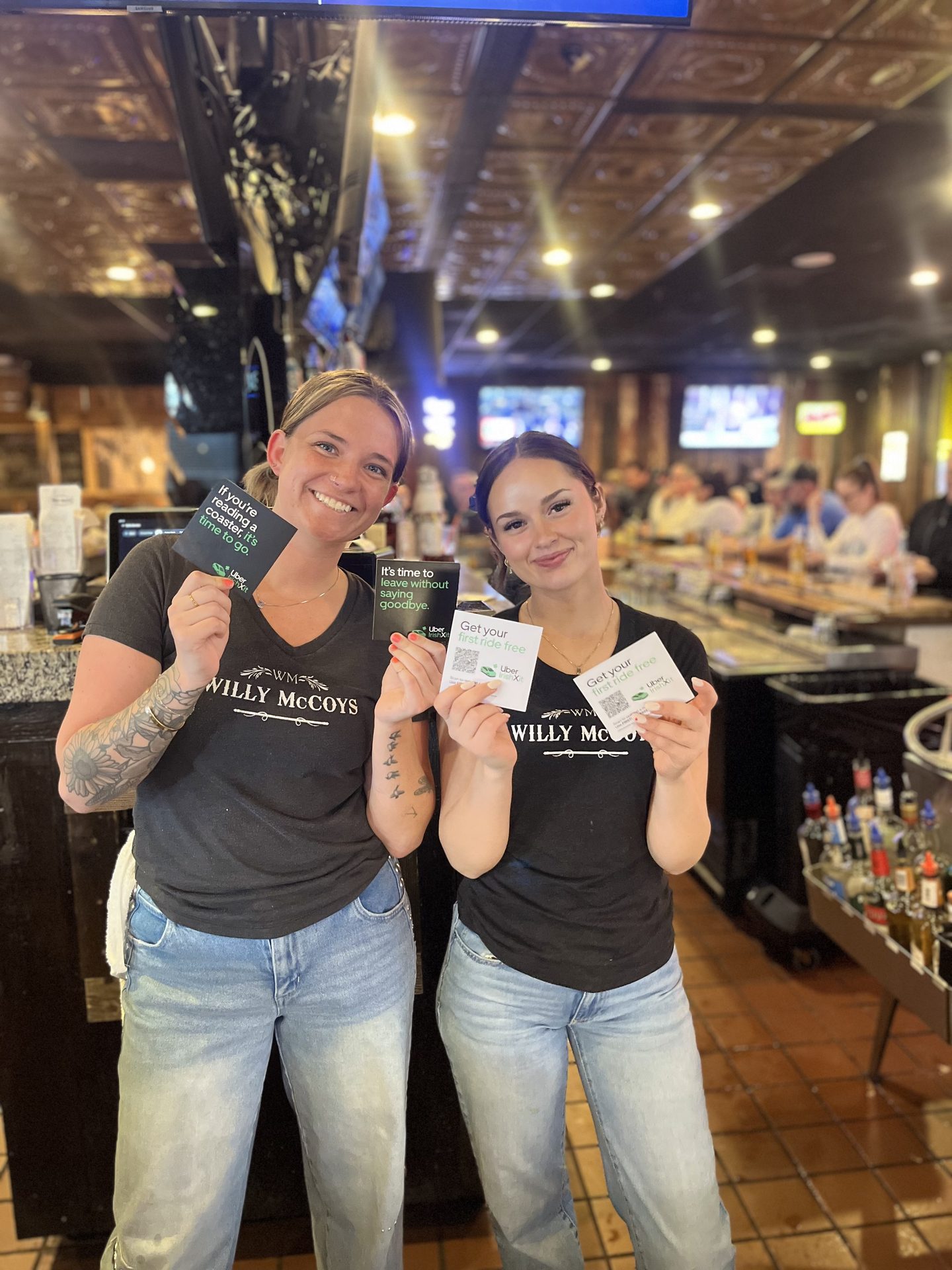 Two Willy McCoy's staff holding Uber Eats coasters at the bar