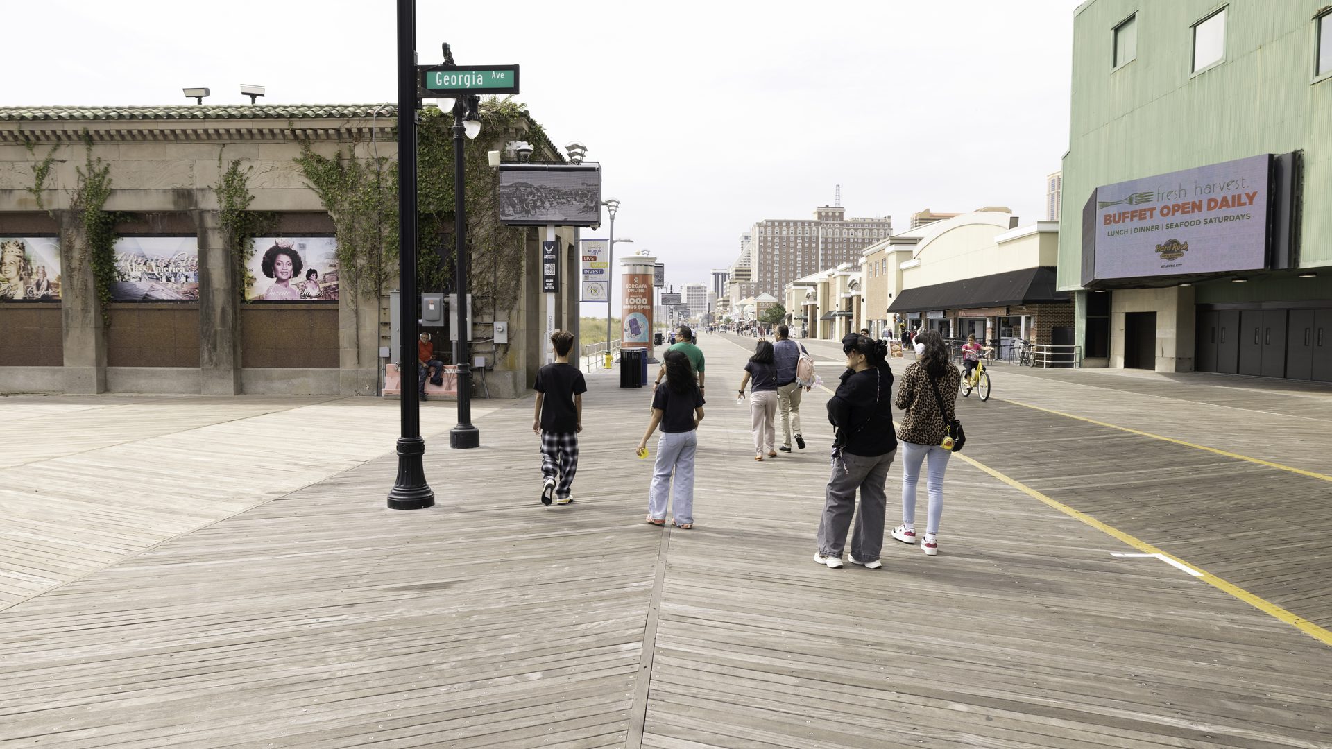 Boardwalk visitors at Georgia Avenue passing APM poster displays, casino towers in the distance
