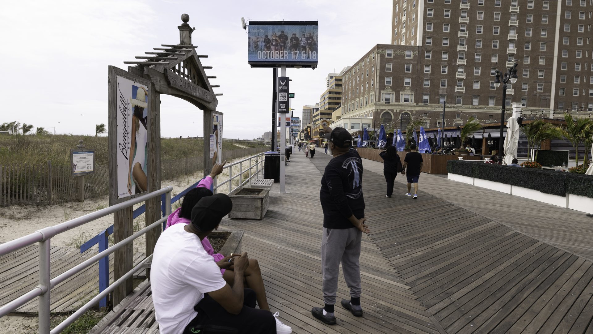 An APM digital screen beside a Boardwalk pergola showing October event dates, with the hotel row behind