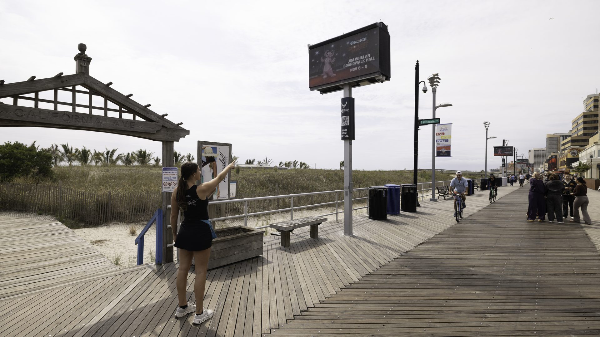 A visitor gesturing toward an APM digital screen beside a Boardwalk pergola