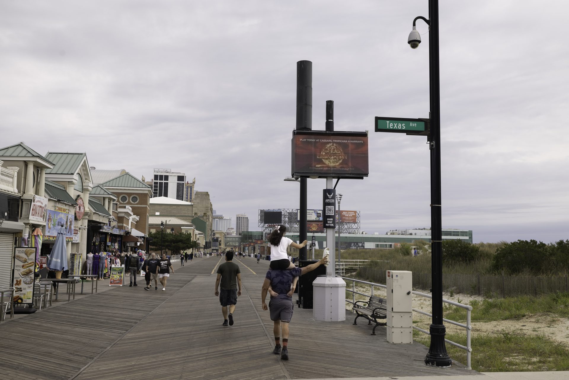 An APM digital screen on the Atlantic City Boardwalk at Texas Avenue, with a child on their father's shoulders reaching toward it