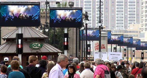 Crowds on the Atlantic City Boardwalk beneath APM digital screens at dusk
